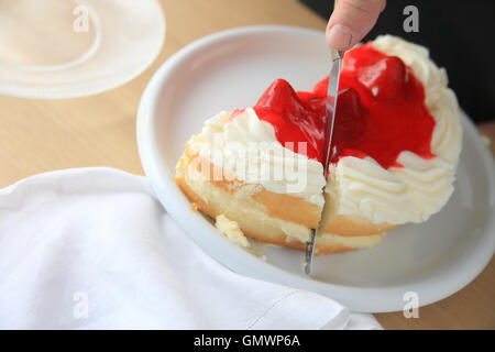 Ein Mann schneidet einen Kuchen mit Pudding, garniert mit Sahne und Erdbeeren gefüllt. Stockfoto