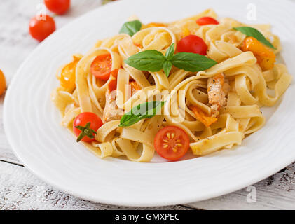 Fettuccine Nudeln in Tomatensauce mit Huhn, Tomaten mit Basilikum auf einem Holztisch dekoriert Stockfoto