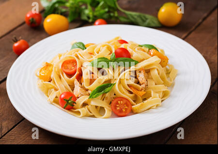 Fettuccine Nudeln in Tomatensauce mit Huhn, Tomaten mit Basilikum auf einem Holztisch dekoriert Stockfoto