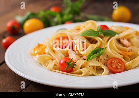 Fettuccine Nudeln in Tomatensauce mit Huhn, Tomaten mit Basilikum auf einem Holztisch dekoriert Stockfoto