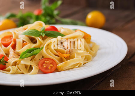 Fettuccine Nudeln in Tomatensauce mit Huhn, Tomaten mit Basilikum auf einem Holztisch dekoriert Stockfoto