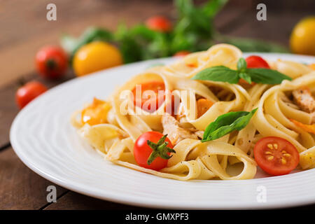 Fettuccine Nudeln in Tomatensauce mit Huhn, Tomaten mit Basilikum auf einem Holztisch verziert. Stockfoto