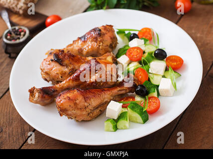 Appetitlich Ofen gebacken golden Chicken Drumsticks und griechischer Salat Stockfoto