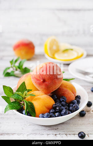 Frische Pfirsiche und Heidelbeeren in Schüssel auf einem hölzernen Hintergrund im rustikalen Stil Stockfoto