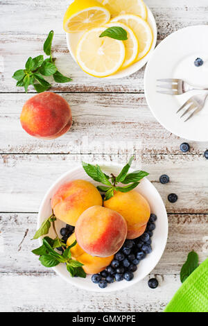 Frische Pfirsiche und Heidelbeeren in Schüssel auf einem hölzernen Hintergrund im rustikalen Stil. Ansicht von oben Stockfoto