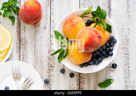 Frische Pfirsiche und Heidelbeeren in Schüssel auf einem hölzernen Hintergrund im rustikalen Stil. Ansicht von oben Stockfoto