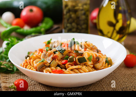 Vegetarische Gemüse-Nudeln Fusilli mit Zucchini, Pilzen und Kapern in weiße Schüssel auf Holztisch Stockfoto