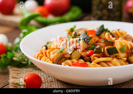 Vegetarische Gemüse-Nudeln Fusilli mit Zucchini, Pilzen und Kapern in weiße Schüssel auf Holztisch Stockfoto