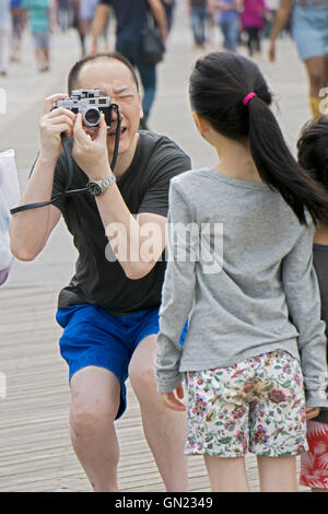 Ein asiatisch-amerikanische Mann nimmt ein Foto seiner Tochter mit einem Vintage Messsucherkamera Leica in Coney Island, Brooklyn, NYC. Stockfoto