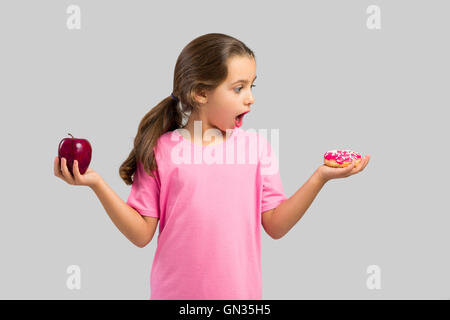 Kleines Mädchen lächelnd und die Wahl zwischen einem Apfel und einen donut Stockfoto