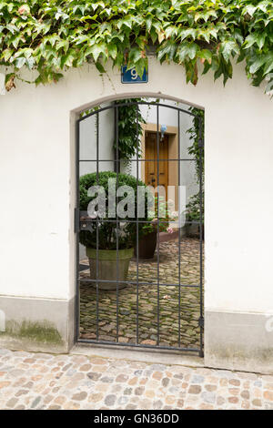 Blick durch ein Tor mit Metallstangen in einem niedlichen kleinen Innenhof. Stockfoto