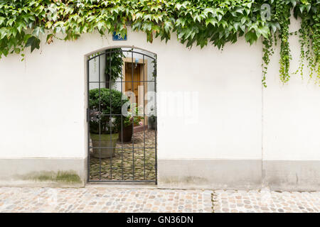 Blick durch ein Tor mit Metallstangen in einem niedlichen kleinen Innenhof. Stockfoto