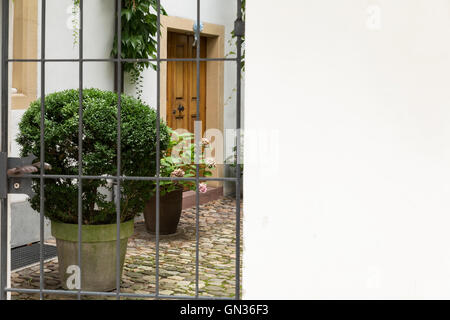 Blick durch ein Tor mit Metallstangen in einem niedlichen kleinen Innenhof. Stockfoto