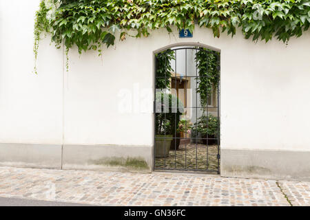 Blick durch ein Tor mit Metallstangen in einem niedlichen kleinen Innenhof. Stockfoto