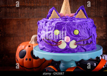 Happy Halloween Kuchen Partei Katzenfutter mit lila Zuckerguss und Süßigkeiten Dekorationen auf dunklem Holz. Stockfoto