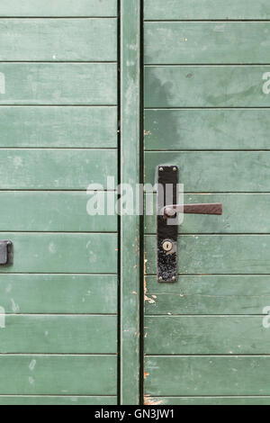 Eine grüne Holztür mit einem abgenutzten Metallgriff und Längsstreifen. Stockfoto