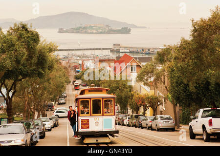 Eine Seilbahn kriecht oben Hyde Street, einer der San Francisco viele steile Straßen mit Alcatraz Island im Hintergrund. San Fra Stockfoto