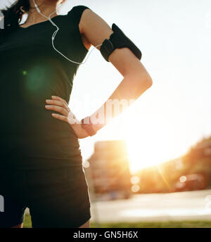 Schuss von Fit Frau stand im Freien mit ihren Händen auf den Hüften beschnitten. Weibliche Läufer tragen Smartwatch Gerät mit Sonne Flare, taki Stockfoto