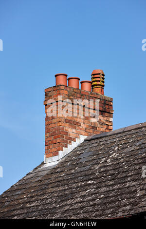 alten viktorianischen Schornstein mit Töpfen auf dem Dach aus einer Reihe von Reihenhäusern vor blauem Himmel im Vereinigten Königreich Stockfoto