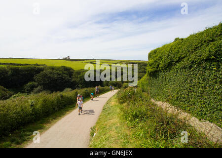 Touristen in Tintagel Castle walk & laufen auf dem steilen hügeligen Weg verbindet die Burganlage der Stadt und Parkhäuser. Stockfoto