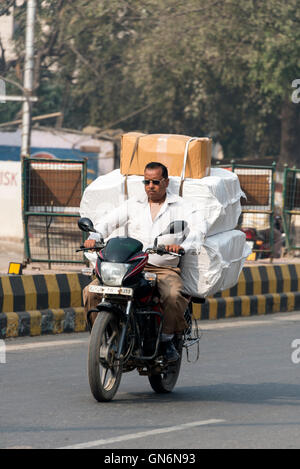 Ein Motorradfahrer, der eine Überladung von Waren auf einer viel befahrenen Hauptstraße in Agra, Uttar Pradesh, Indien, trägt Stockfoto