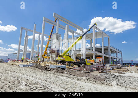 Mobiler Kran arbeitet daran, große Montagehalle. Platzieren den Dachstuhl auf den Aufbau von Skelett. Stockfoto