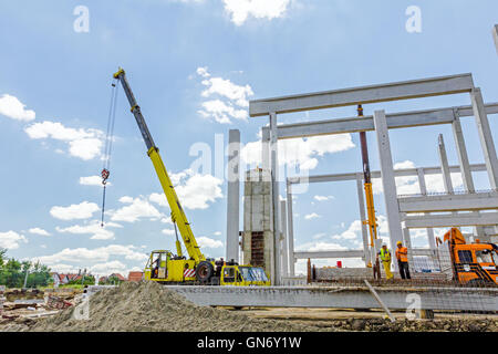 Mobiler Kran arbeitet daran, große Montagehalle. Platzieren den Dachstuhl auf den Aufbau von Skelett. Stockfoto