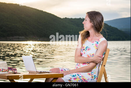 Nachdenkliche Frau mit Laptop am See Stockfoto