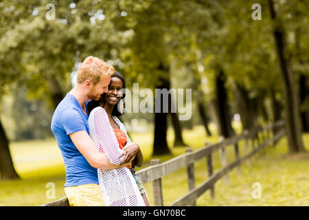 Junge gemischtrassige paar in Liebe stand neben dem Zaun im Park an einem sonnigen Tag Stockfoto