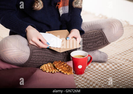 Weiche gemütliche Foto von schlanke Tan Frau in warmen Pullover auf dem Bett mit Tee in Händen, Ansicht von oben Punkt. Komposition mit warmen Plaid, Umschlag, Tasse Heißgetränk und weibliche Beine Stockfoto