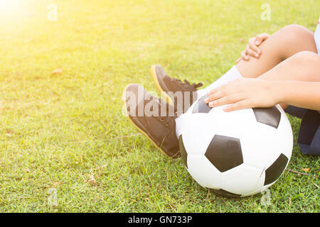 Junge sitzt auf dem grünen Rasen mit einem Fußball in der Hand. Nahaufnahme Stockfoto