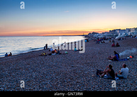 Menschen sitzen auf Brighton Beach bei Sonnenuntergang, Brighton, Sussex, UK Stockfoto