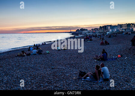 Menschen sitzen auf Brighton Beach bei Sonnenuntergang, Brighton, Sussex, UK Stockfoto
