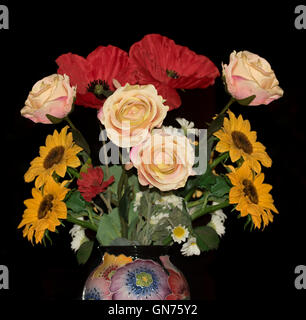 Anordnung der bunten Kunstblumen, rote Mohnblumen, goldene Sonnenblumen & rosa Rosen in floral Keramikvase auf schwarzem Hintergrund Stockfoto