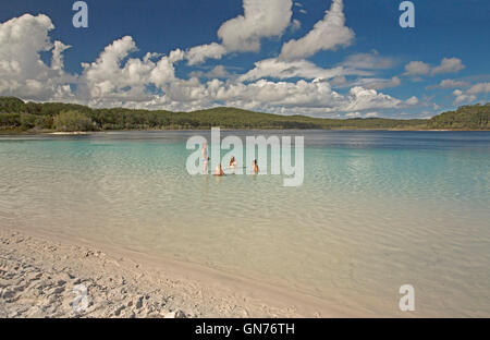 Lake Mackenzie mit Gruppe von Touristen im türkisfarbenen Wasser über weißen Sand gesäumt von Wäldern & unter blauem Himmel auf Fraser Island Stockfoto