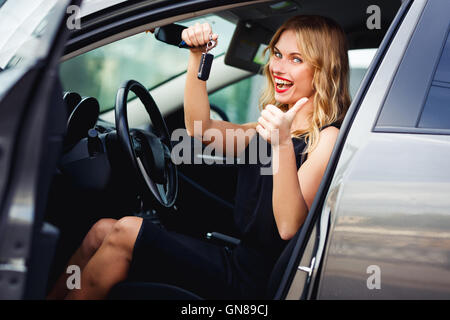 Fröhliche Blondine im Auto, Schlüssel und Daumen auftauchen Stockfoto