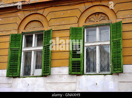 Holz Fenster mit den grünen Vorhängen an der gelben Wand Stockfoto