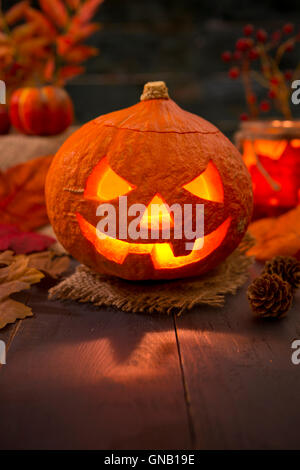 Brennen von Jack O'Lantern auf einem rustikalen Tisch mit herbstlichen Dekorationen, beleuchtet dunkel. Stockfoto