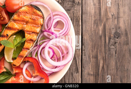 Gegrilltes Lachssteak mit in Scheiben geschnittenen Zwiebeln und Tomaten auf der linken Seite Stockfoto