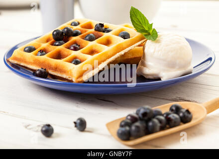 Belgische Waffeln mit Heidelbeeren und Vanilleeis Kugel auf der blauen Platte auf rustikalen Holztisch, geringe Schärfentiefe Stockfoto