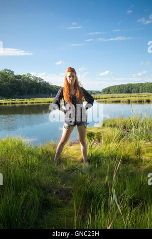 Junge Frau mit langen roten Haaren stehen auf der Hut in einem ruhigen Sumpf im Sommer trägt Shorts und ein t-Shirt. Stockfoto