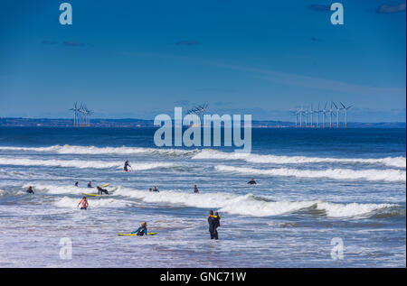 Surfer in weißen Wellen mit Windpark in Ferne Stockfoto