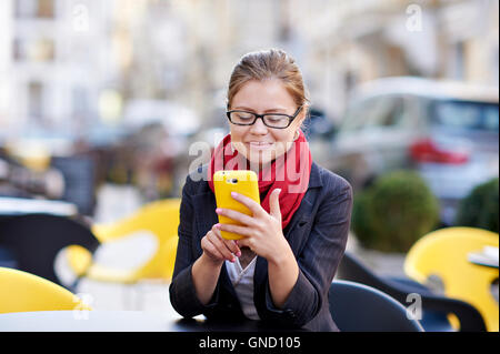 junge Frau in Gläsern schreibt Sms auf Handy Stockfoto