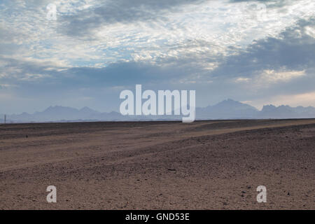 Flache sandige Gelände in der Wüste in Ägypten, in der Nähe der Küste und Stadt Hurghada. Linie der Berge im Hintergrund. Intensive c Stockfoto