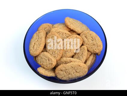 Cookies in einem blauen Glasschale. Stapel der ovalen hausgemachten Butter Cookies in einem runden blauen durchsichtigen Glas Teller, auf weißem Hintergrund, Ansicht von oben. Stockfoto