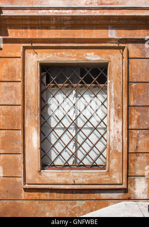 Fenster eines alten Gebäudes in der Stadt von Rom, Italien. Fenster wird durch diagonal Gitter geschützt. Terrakotta-Farbe des Hauses, ty Stockfoto