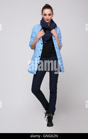 Junge Frau in eine blaue Jacke mit einem Schal um den Hals und Hosen, posiert im Studio in voller Länge. Mode. Stockfoto