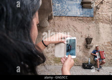 Ein Tourist zeichnet ein Straßenkünstler sein Akkordeon spielen und singen in Obidos, Portugal. Stockfoto