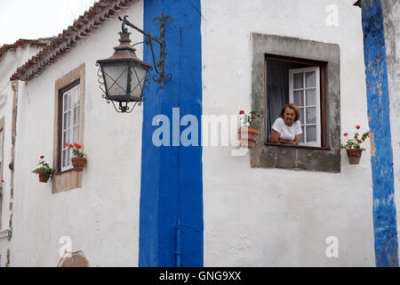 Eine Frau schaut aus ihrem Fenster in mittelalterlichen Mauern umgebene Stadt Obidos, Portugal. Stockfoto