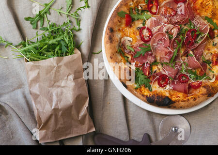 Parma-Schinken-Pizza mit Rucola und Papier Tasche mit Rucola Stockfoto